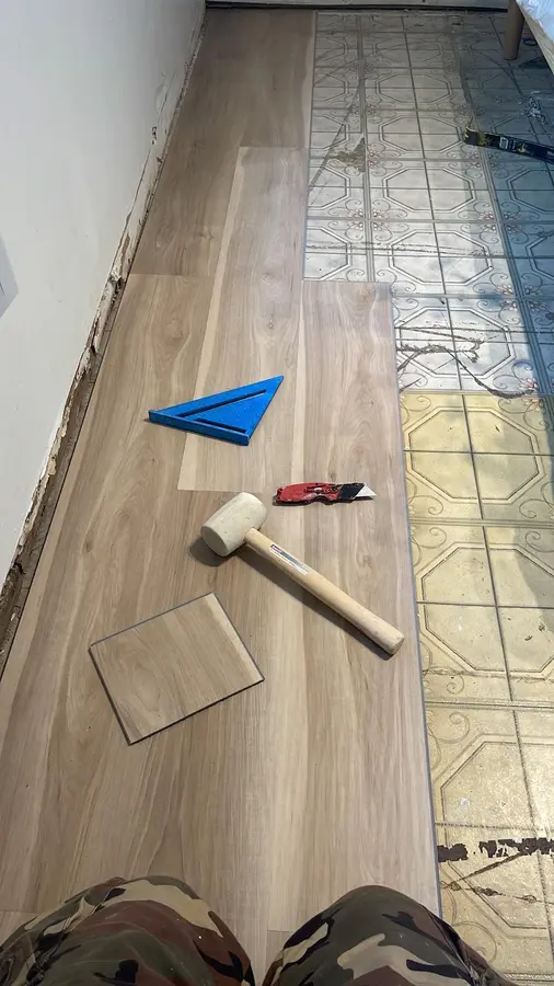 Rigid-core vinyl plank being installed over old tile, with a mallet and a square on the new floor